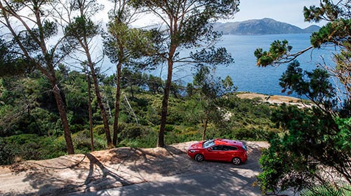 un'auto rossa parcheggiata lungo una strada vicino a uno specchio d'acqua