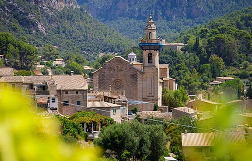 un grande edificio con una torre, circondato da alberi e colline