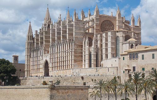 Un grande edificio in pietra con torri e la cattedrale di Palma sullo sfondo